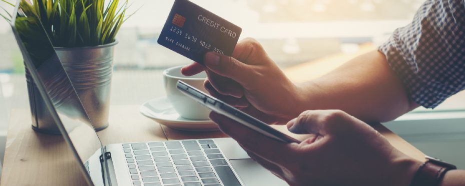 Notebook aberto e pessoa com celular em uma das mãos e cartão de crédito na outra realizando compra em um marketplace B2B.