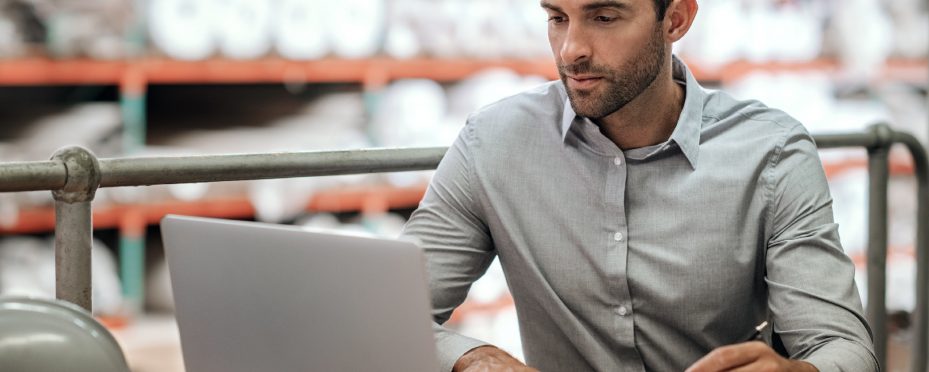 Homem sentado utilizando um notebook em um estoque.
