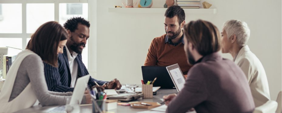 Grupo de pessoas sentado em frente a uma mesa sorriem enquanto conversam sobre anunciar na internet.
