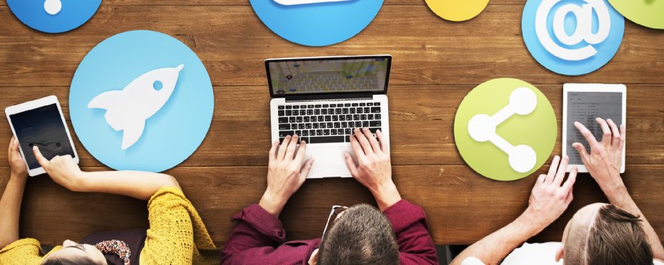 Três pessoas sentadas utilizando tabletes e um notebook para fazer divulgação online.