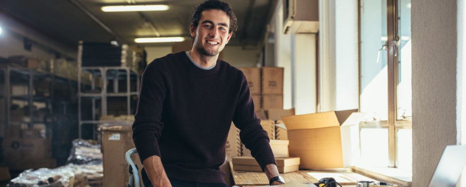Homem de pé sorrindo em um estoque de produtos vendidos no portal B2B.