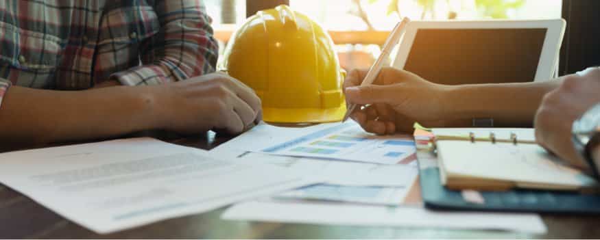 Pessoas sentadas fazendo anotações sobre marketing para indústria e capacete amarelo ao fundo.