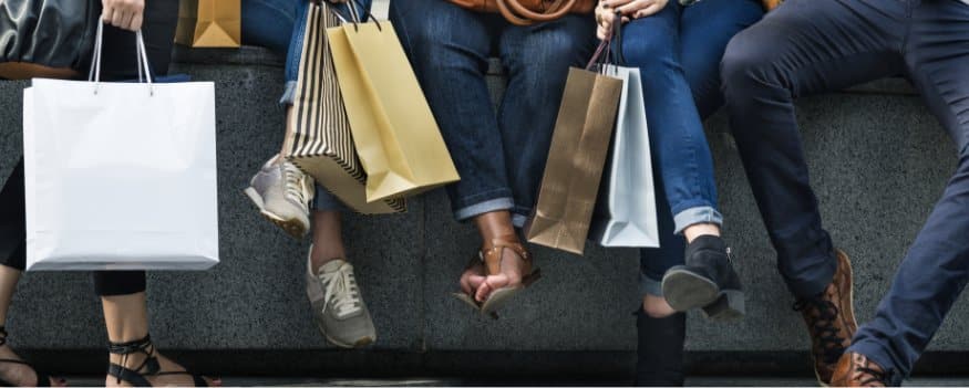 Pessoas sentadas com as pernas balançando e segurando sacolas de compras.