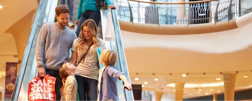 Família descendo escada rolante de shopping center após compras em promoção de vendas.