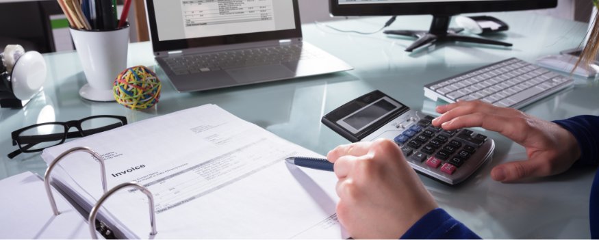 Mãos fazendo usando calculadora sobre mesa com notebook e caderno de anotações sobre como montar um plano de negócios.