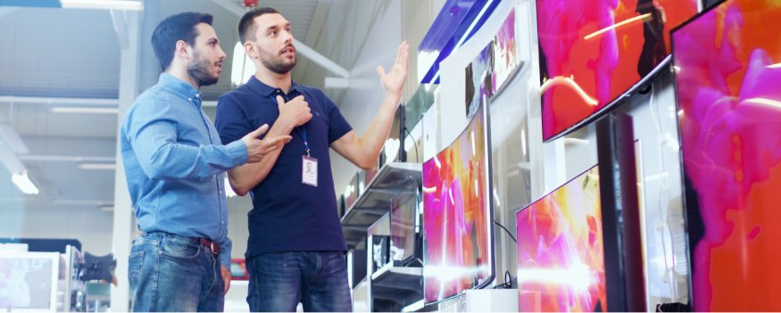 Vendedor e cliente em loja de eletrodomésticos quebrando objeções em vendas em frente a televisores.