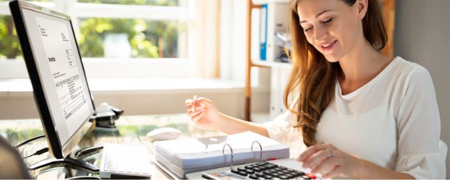 Mulher fazendo anotações e cálculos em frente ao computador para descobrir o ativo circulante.