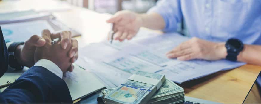 Homens sentados frente a frente finalizando empréstimo para empresa com o recebimento do dinheiro.