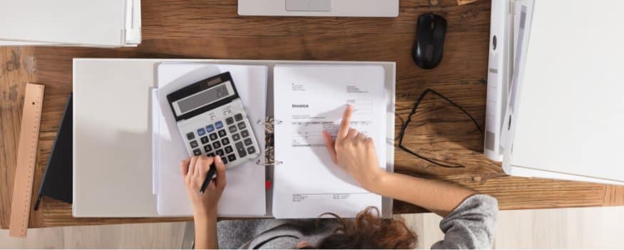 Uma mulher fazendo conta na calculadora e consultando um caderno.