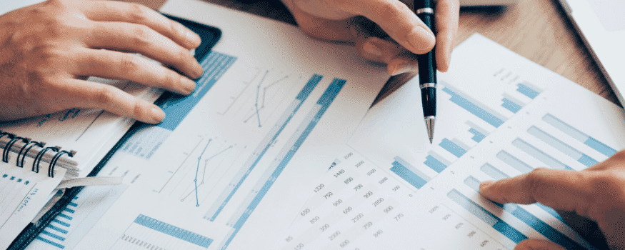 Pessoas analisando gráficos com uma lapiseira.