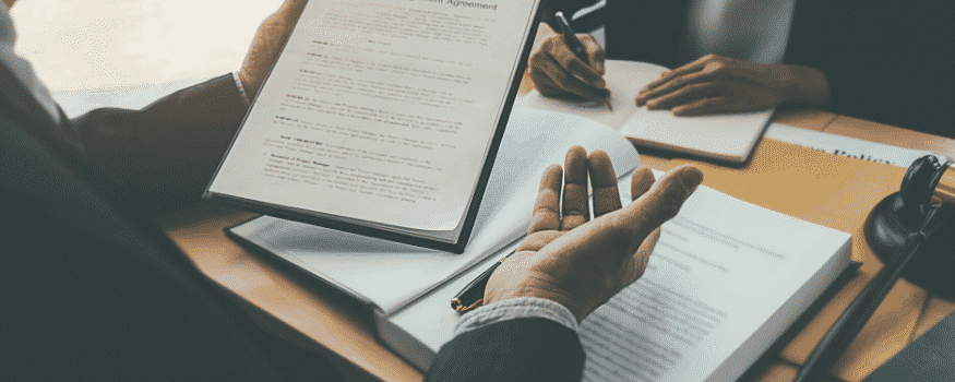 Duas pessoas conversando sobre o contrato de serviço enquanto um assina um papel e o outro analisa outro.