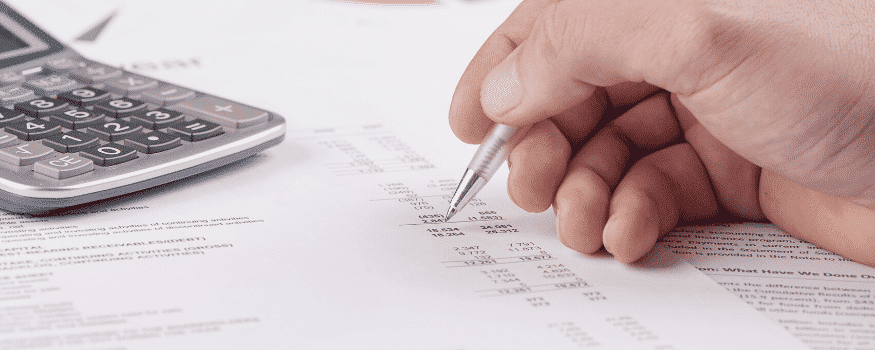 Uma pessoa fazendo anotações referente ao controle financeiro empresarial com uma calculadora do lado.