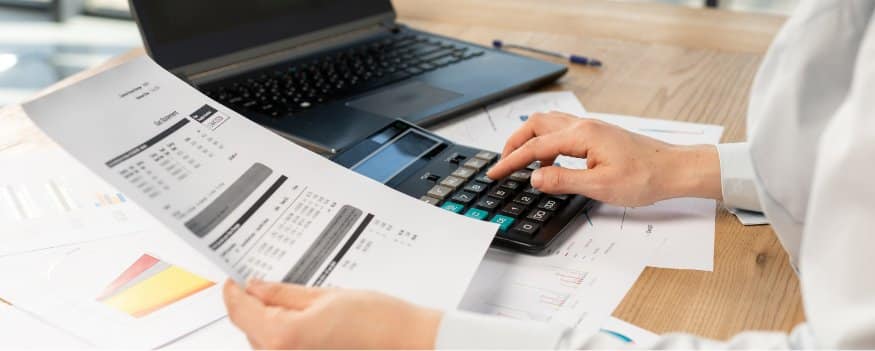 Uma pessoa fazendo cálculos em uma calculadora e verificando algumas folhas.