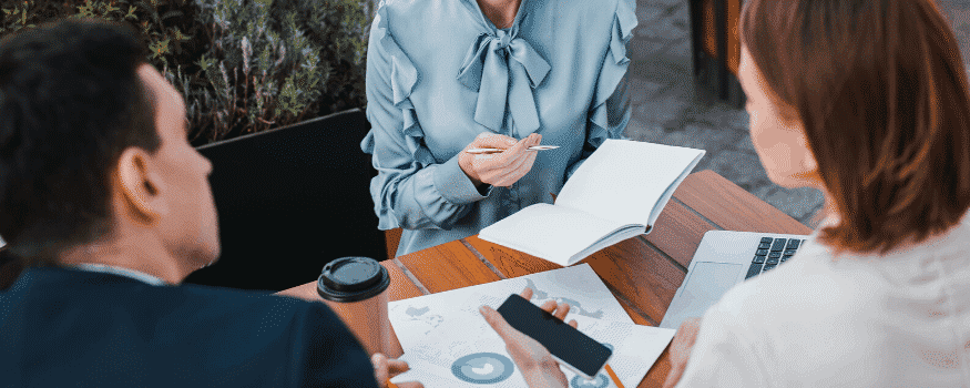 Três pessoas fazendo uma reunião e colhendo informações de gráficos, celulares e notebooks.