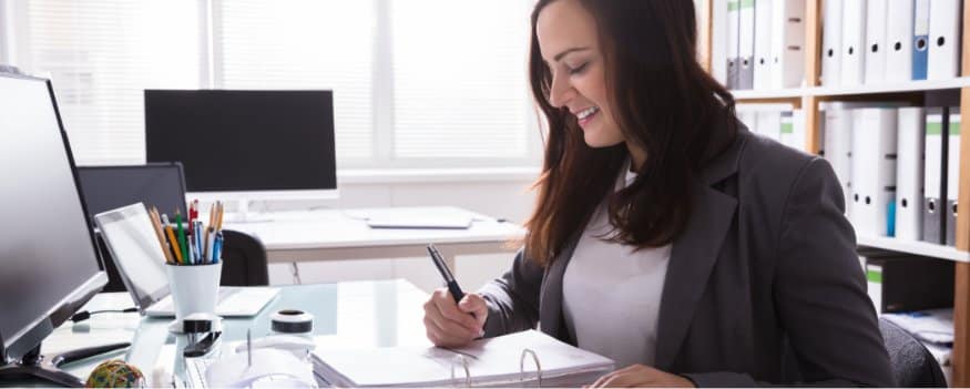Uma mulher realizando o regime de competência com um computador e um caderno.