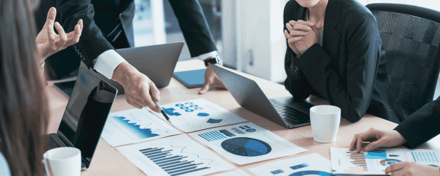 Cinco pessoas em uma reunião tratando sobre estratégia competitiva e desenvolvendo estratégias.
