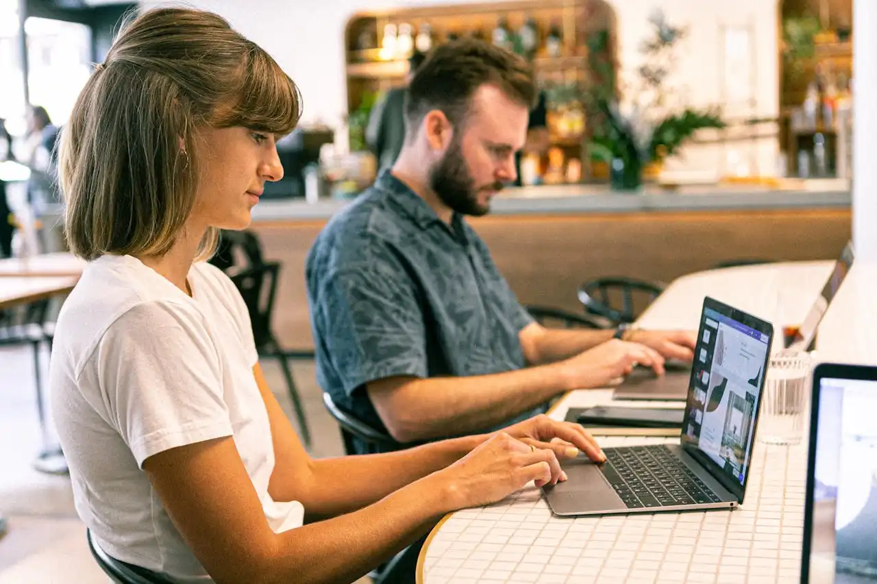 Homem e mulher usando laptops em um espaço de coworking, representando o uso de ferramentas de TI no cenário atual para marketing digital